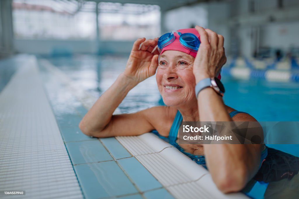 A happy senior woman in swimming pool, leaning on edge.